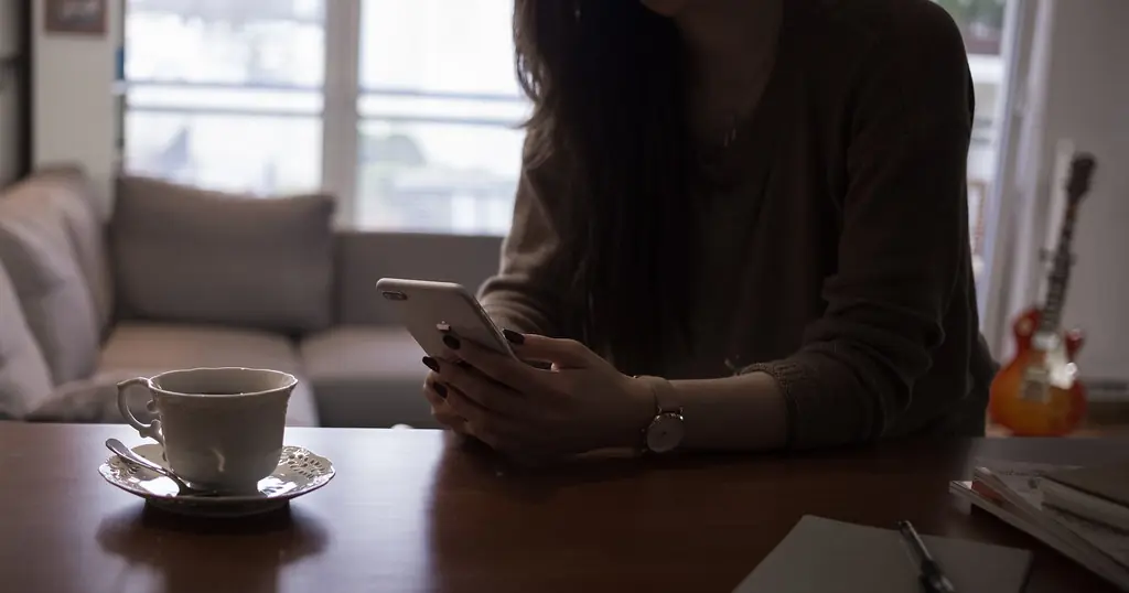 Premier message sur un site de rencontre: une femme lit sur son téléphone à côté d’une tasse