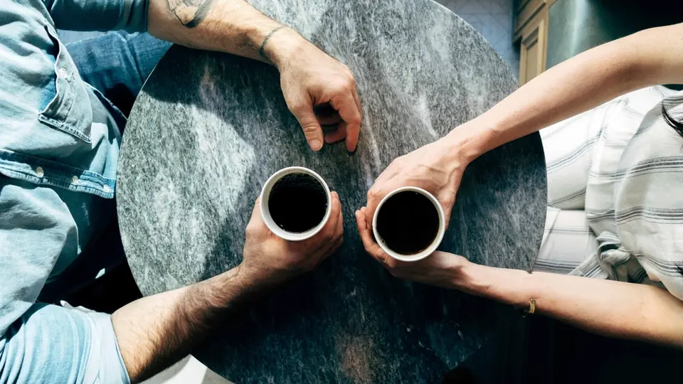Premier rendez-vous: deux tasses de café sur une table ronde en marbre, tenues par deux mains, vues d’en haut